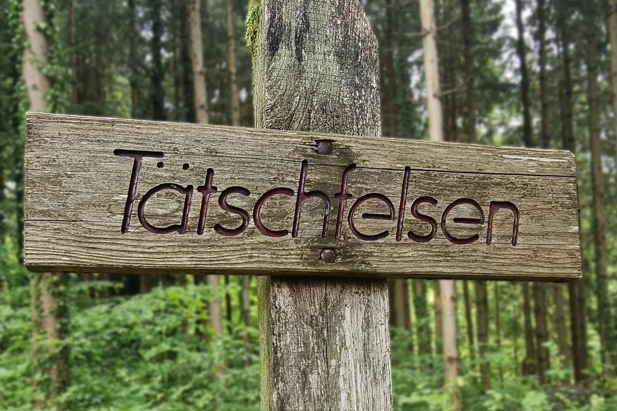 Ein schmaler Weg im Wald führt zum Tätschfelsen, in dessen Nähe ein Mini-Wasserfall ist. Eine Tafel beschriftet mit «Tätschfelsen».